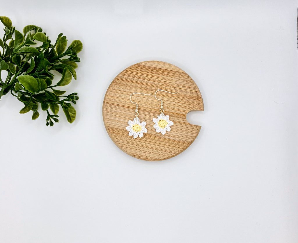 Crochet daisy earrings laying flat on a wood surface