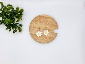 Crochet daisy earrings laying flat on a wood surface