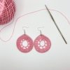 Pink crochet dream catcher earrings next to a ball of pink yarn and a crochet hook
