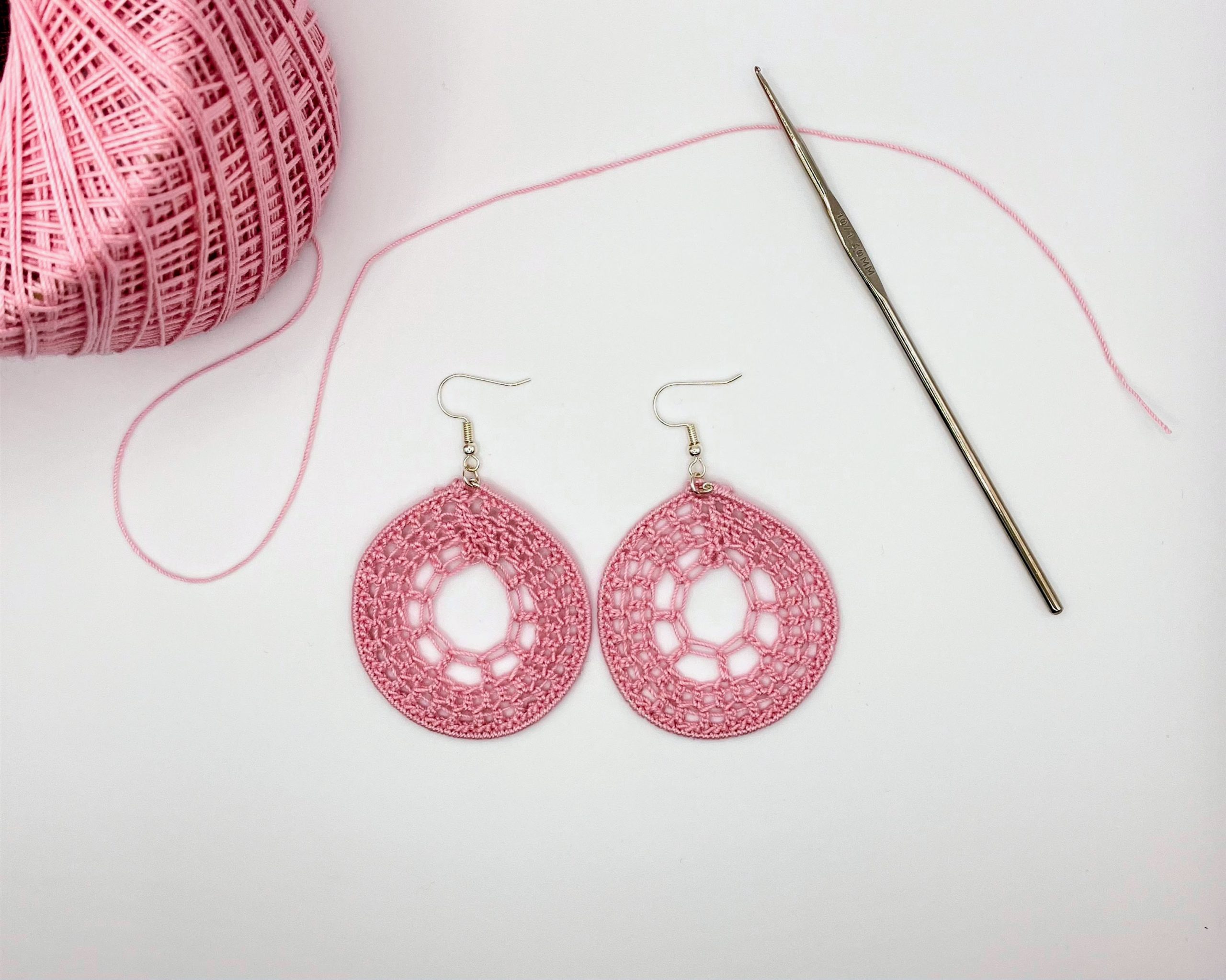 Pink crochet dream catcher earrings next to a ball of pink yarn and a crochet hook