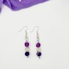Pair of purple and white beaded dangle earrings laying on a white backdrop