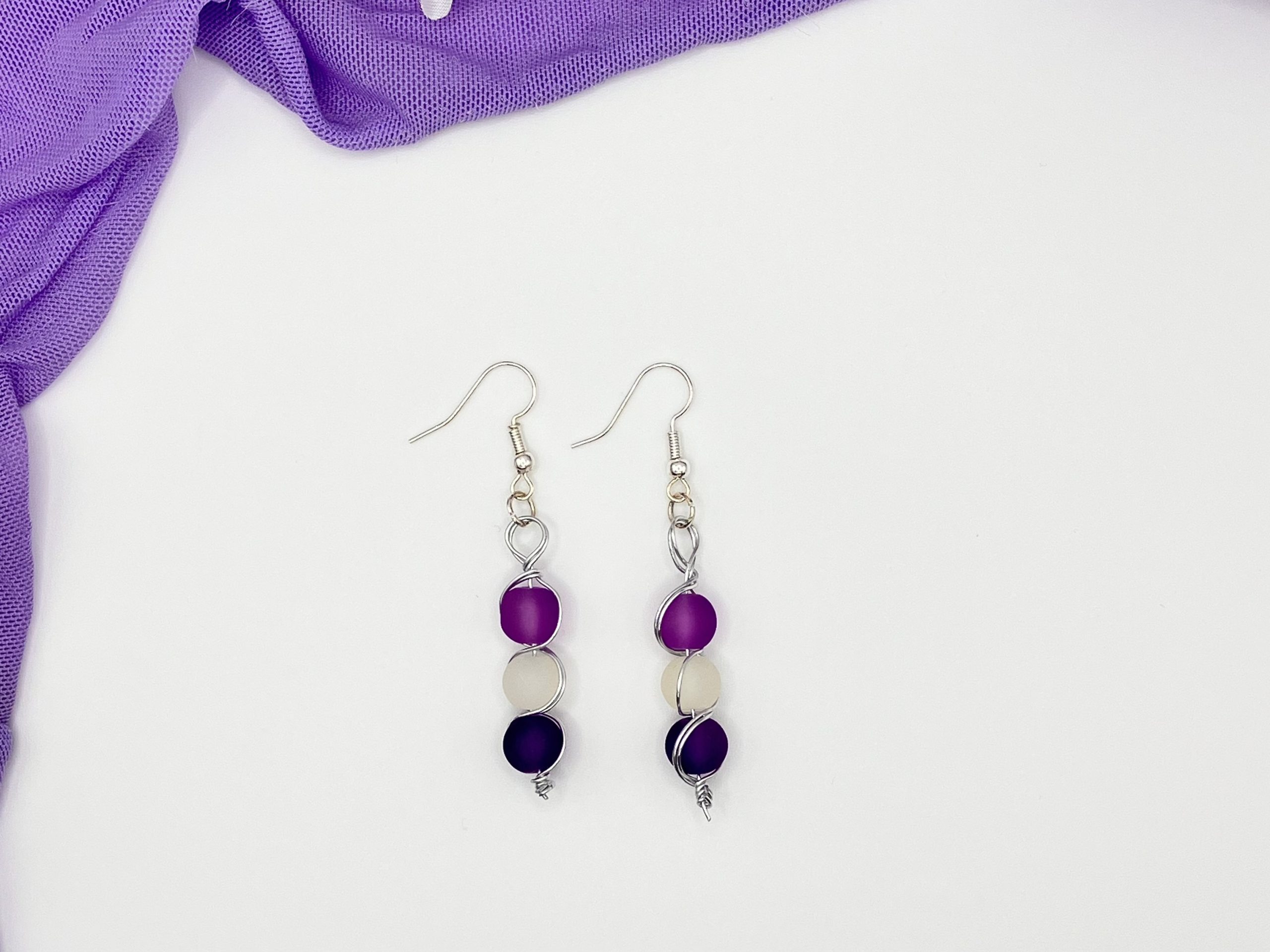 Pair of purple and white beaded dangle earrings laying on a white backdrop