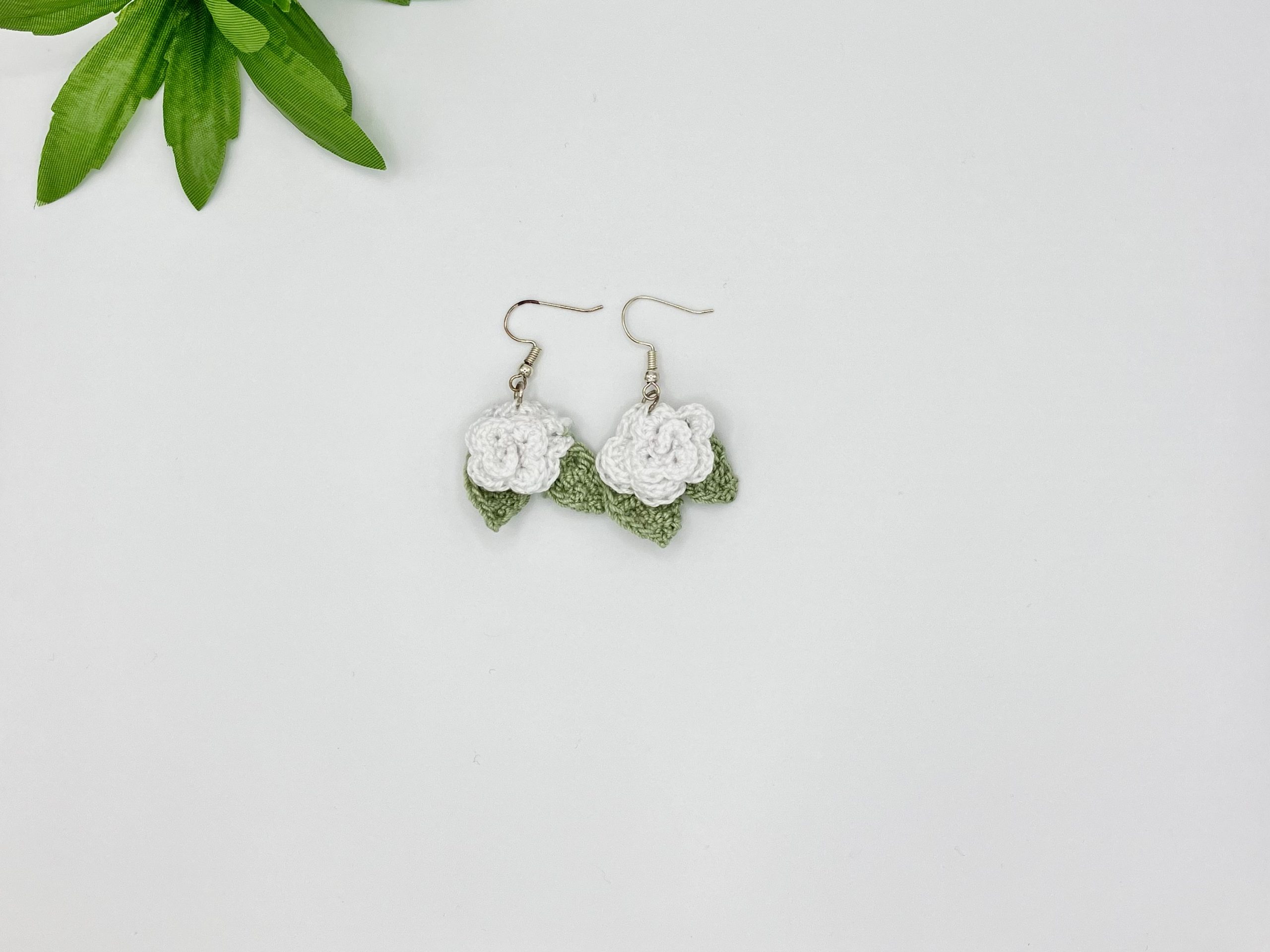 White crochet rose earrings laying flat on a white backdrop