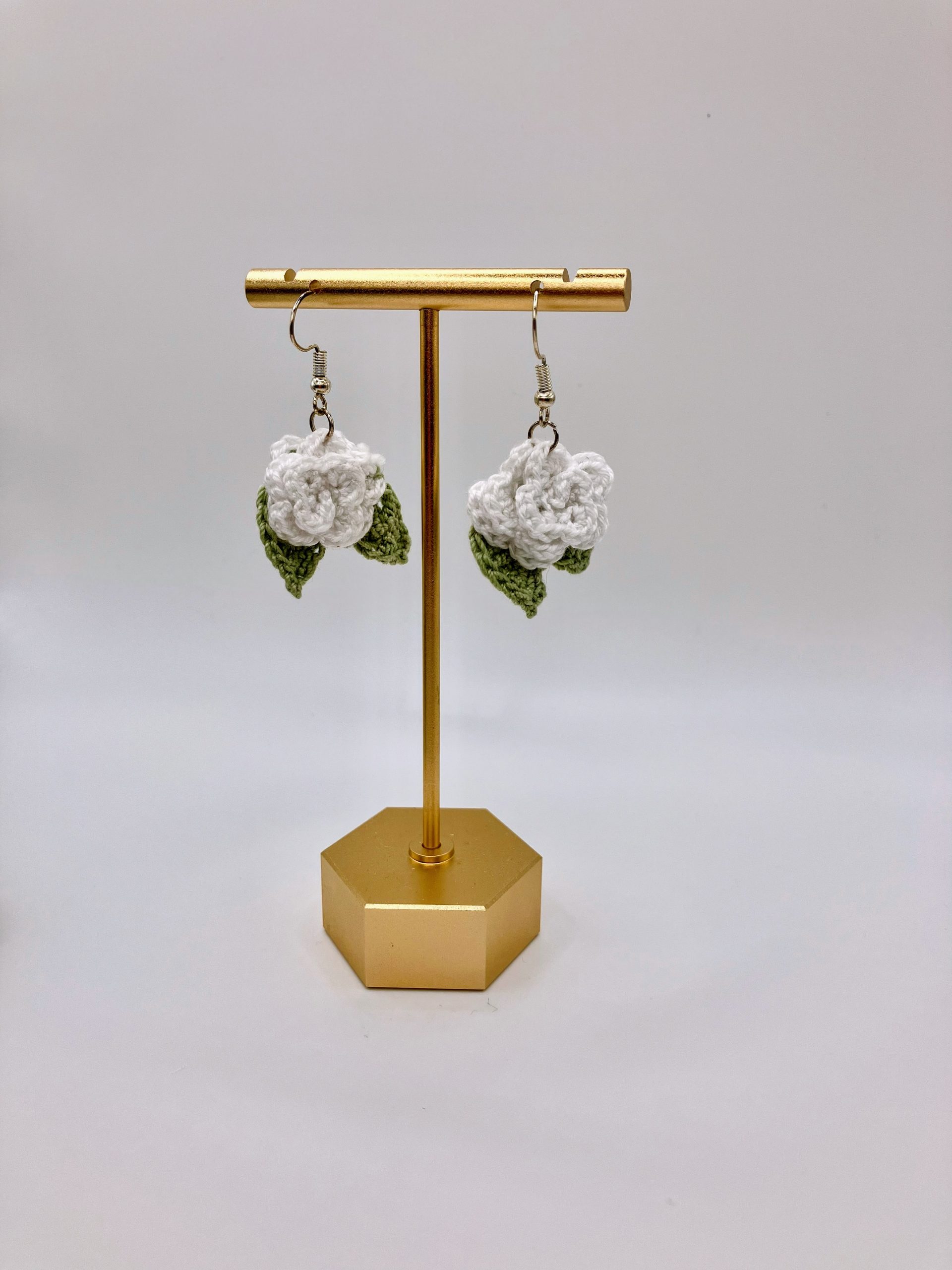 Crochet white rose earrings hanging on a gold earring stand