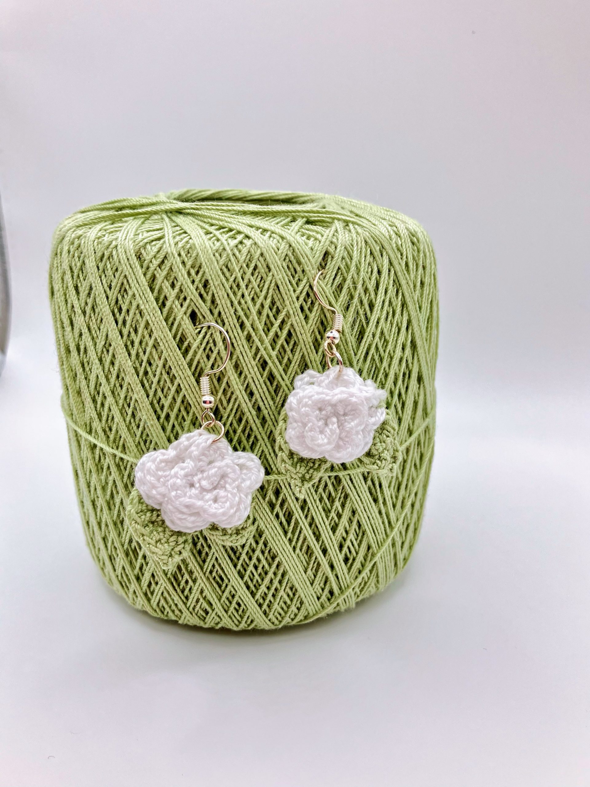 White crochet rose earrings hanging on a ball of green yarn