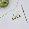 White crochet rose earring next to a ball of green yarn and a crochet hook