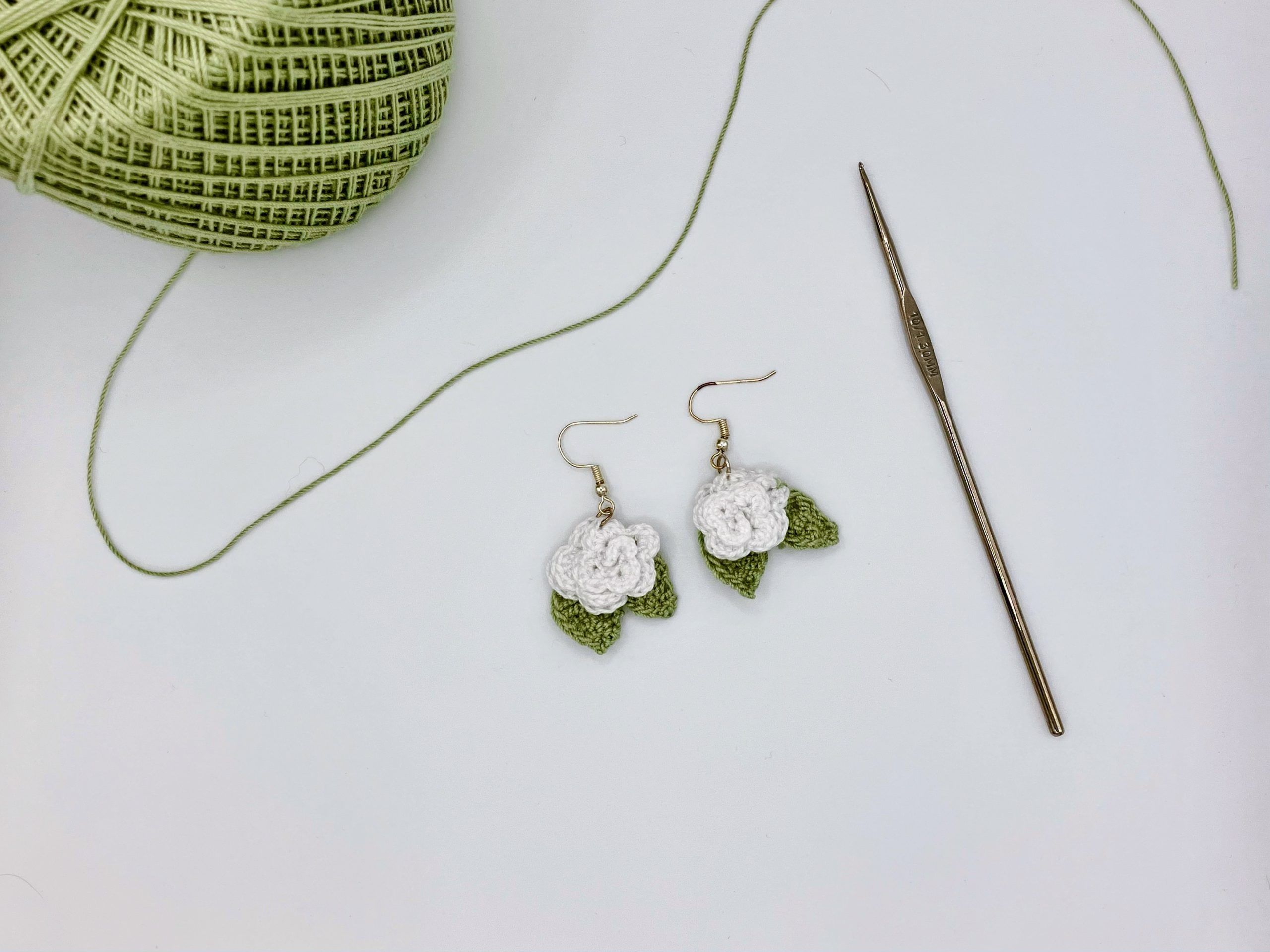 White crochet rose earring next to a ball of green yarn and a crochet hook