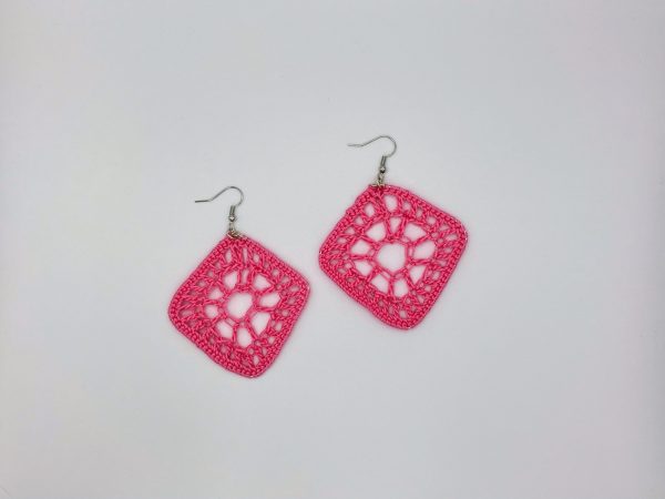 Crochet pink diamond shaped earrings laying next to each other on a white backdrop