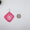 Crochet pink driamond shaped earring laying next to a quarter for reference