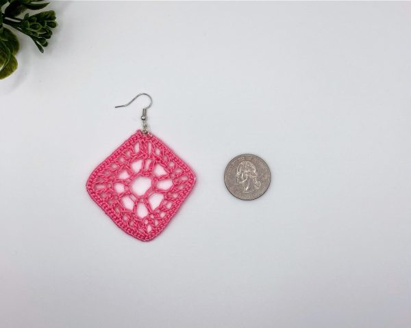 Crochet pink driamond shaped earring laying next to a quarter for reference