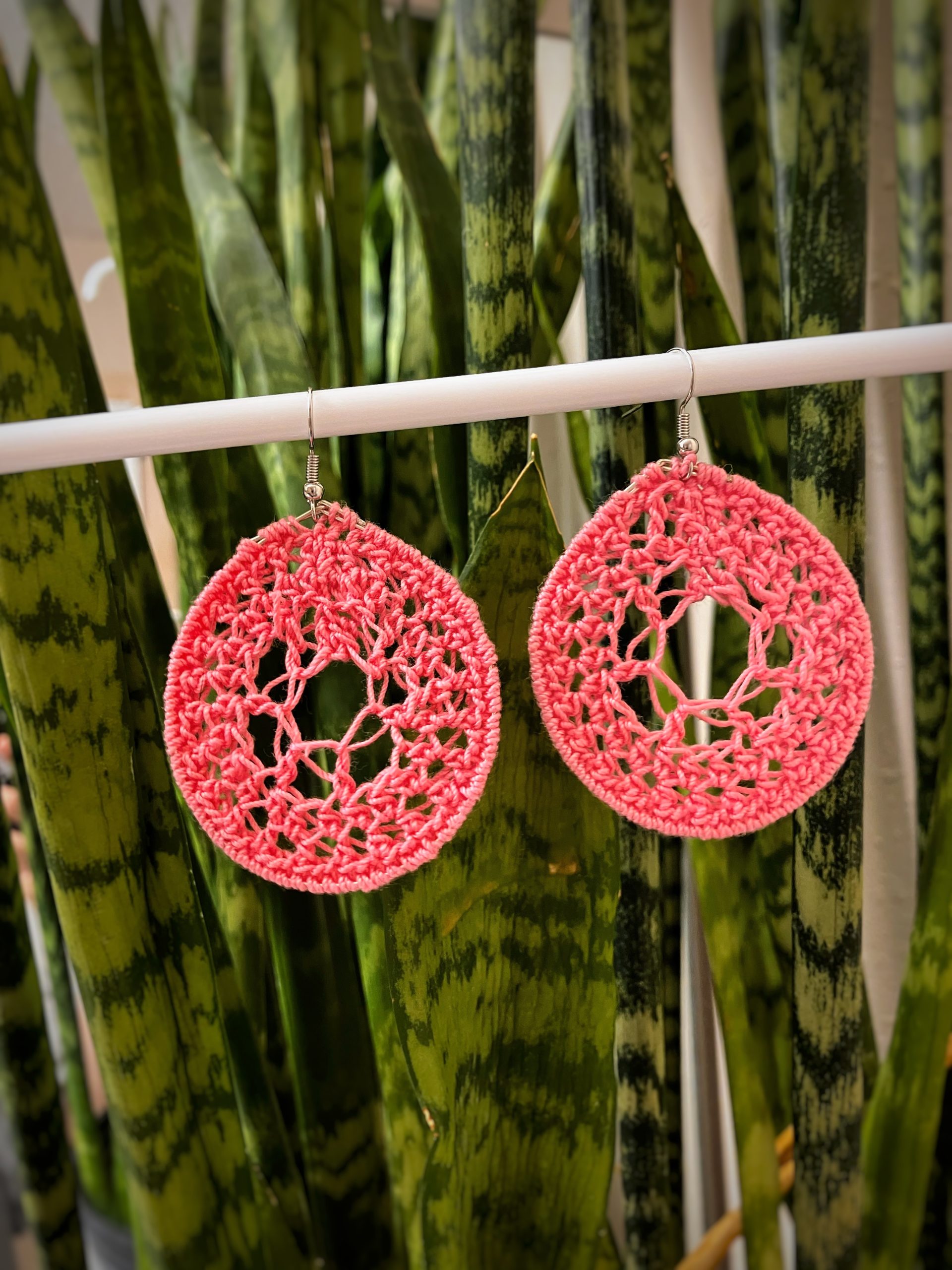 Crochet Dark Pink dream catchers hanging on a white bar in front of a green plant