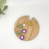 Crochet purple flower bag charm with pearl and gold key ring on a wood coaster