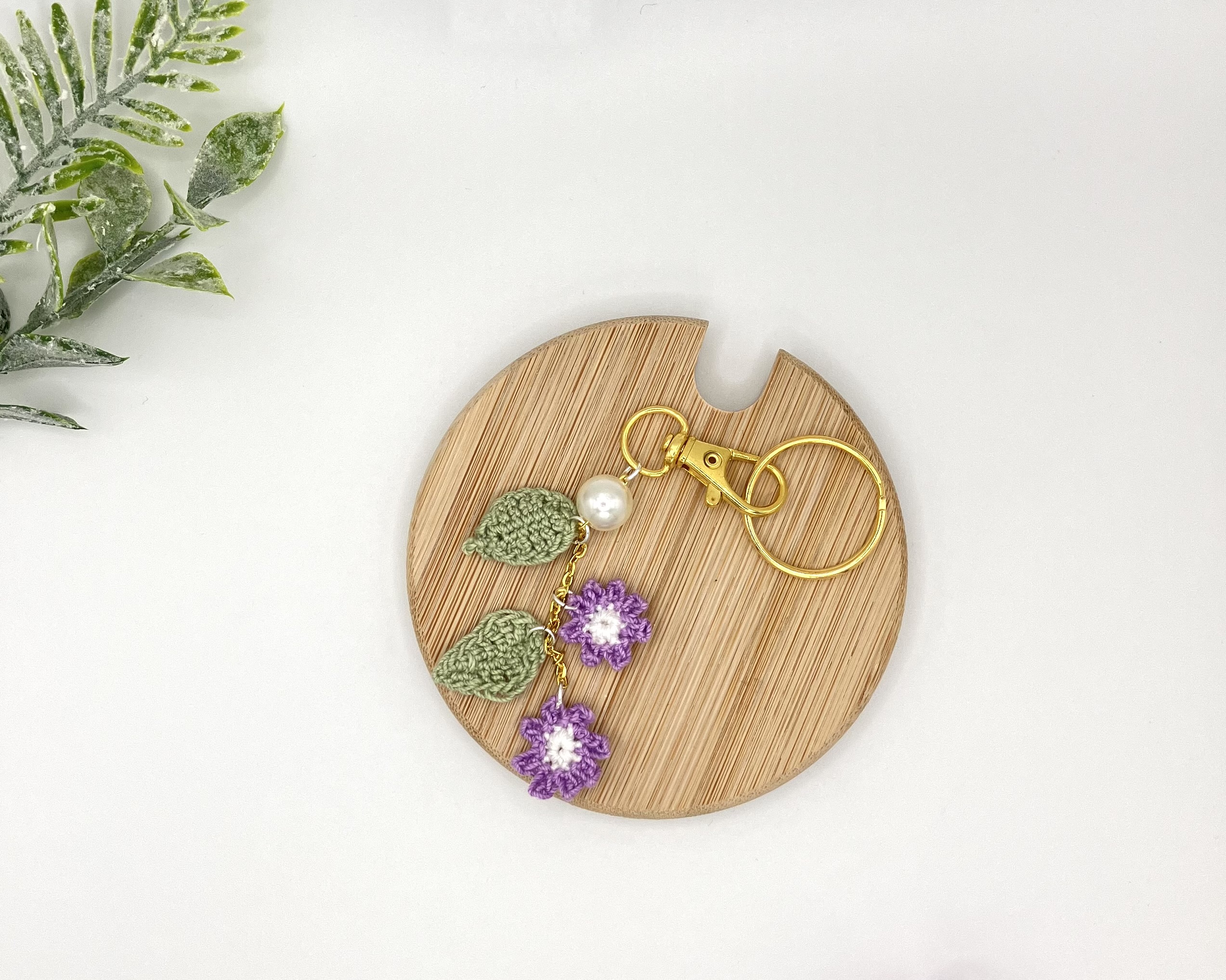 Crochet purple flower bag charm with pearl and gold key ring on a wood coaster
