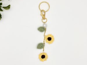 Crochet handmade sunflower bag charm, on a gold chain, with leaves, two flowers, pearl accent