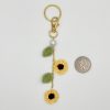 Crochet sunflower gold bag charm with pearl accent, next to a quarter