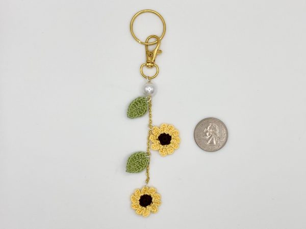 Crochet sunflower gold bag charm with pearl accent, next to a quarter