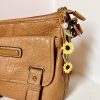 Crochet sunflower bag charm with two sunflowers, pearl accent, and leaves, on a brown purse