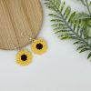 Crochet sunflower earrings with the silver earrings hooks resting on a wood backdrop, and the flower part on white backdrop