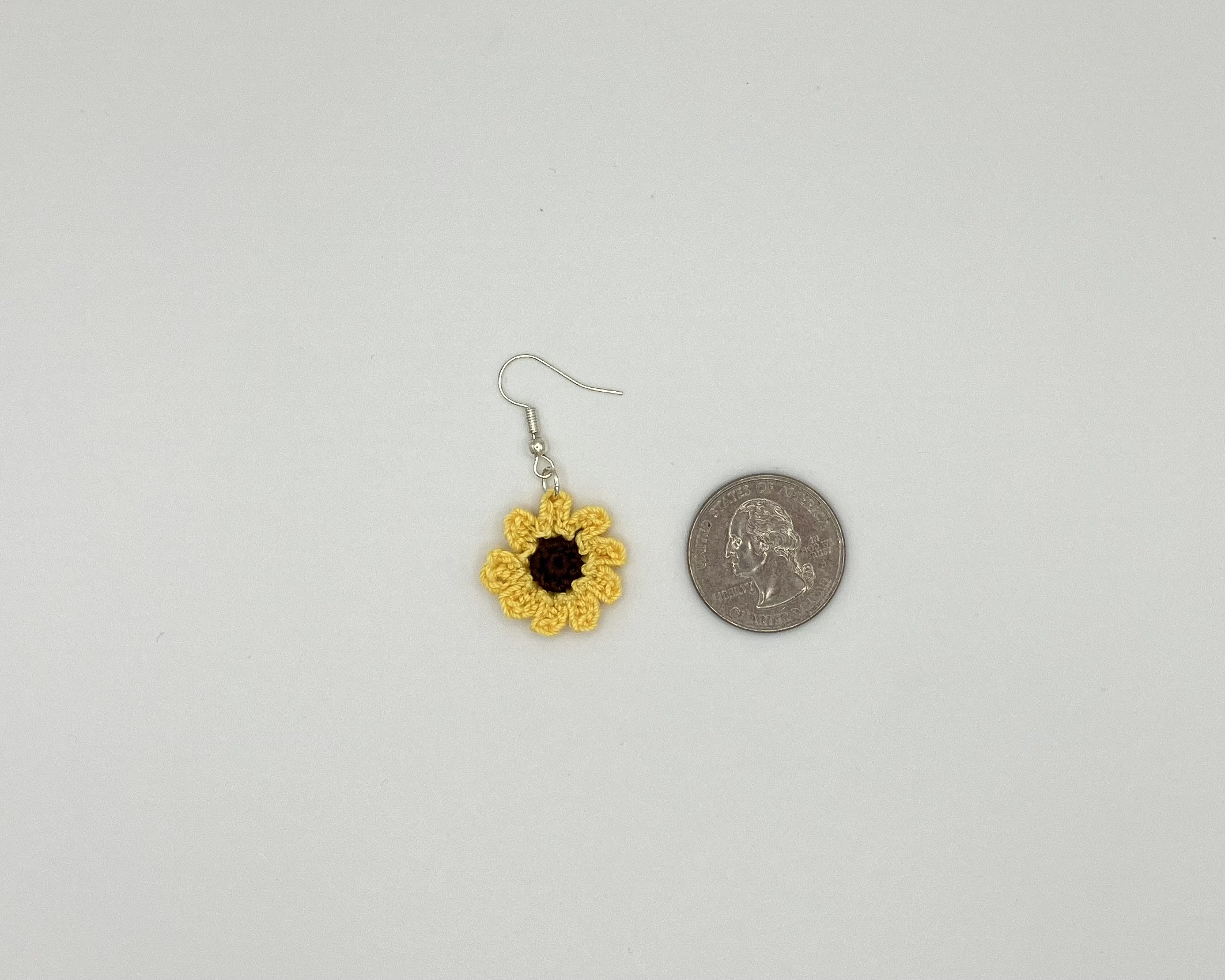 Crochet sunflower earring laying next to a quarter for reference