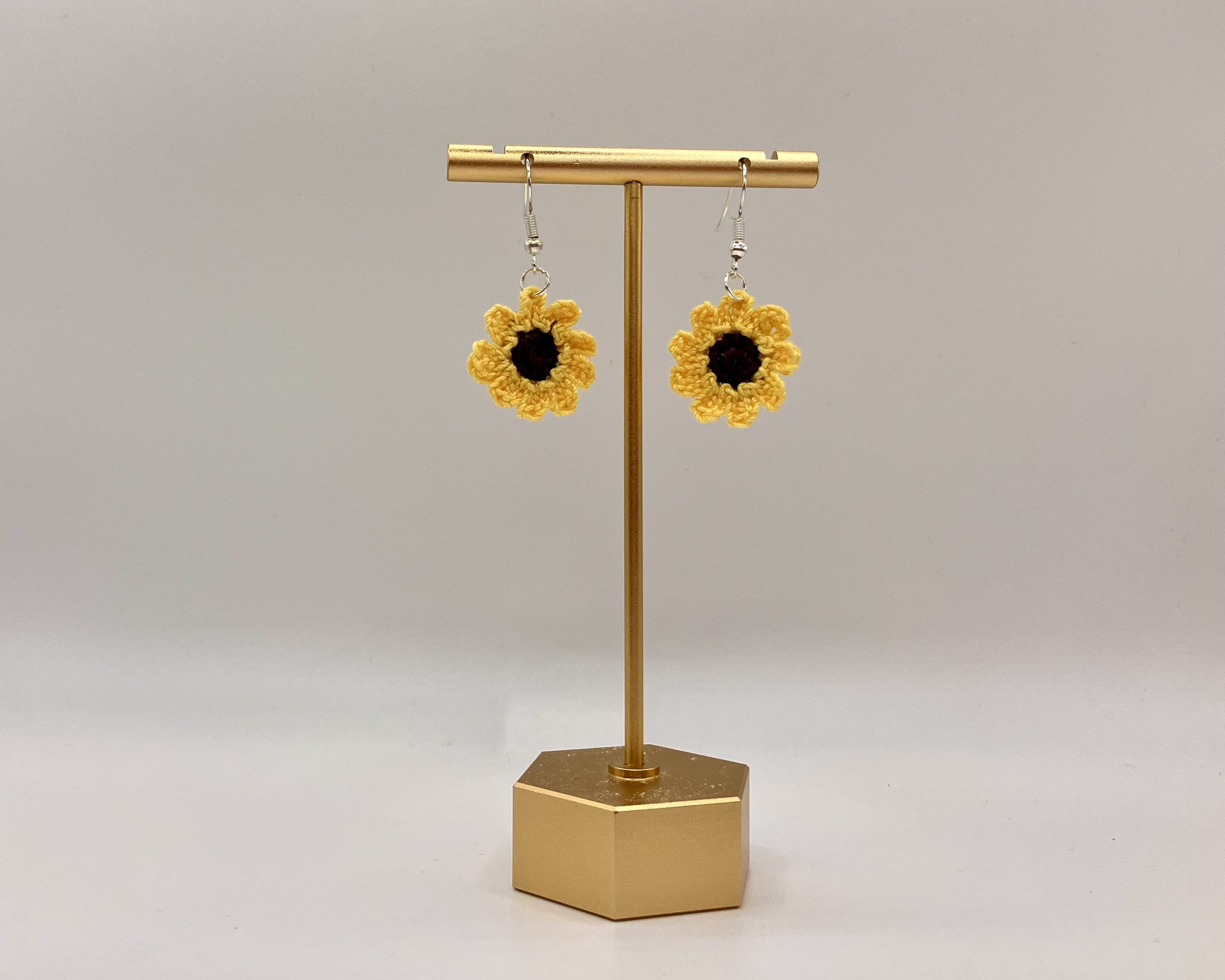 Crochet sunflower earrings hanging on a gold earrings stand