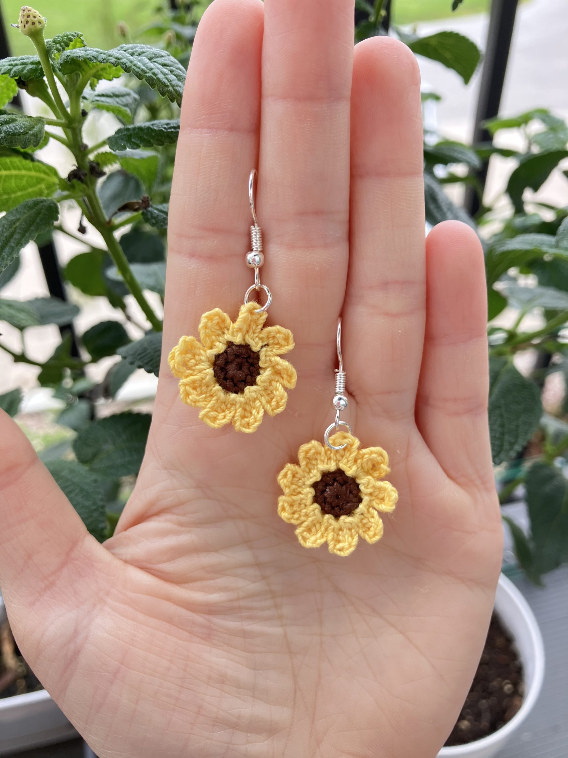 Crochet sunflower earrings in a hand for reference