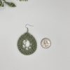 A crochet green dream catcher earring laying next to a quarter for reference