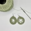 Crochet green dream catcher earrings laying next to a ball of green yarn and a crochet hook