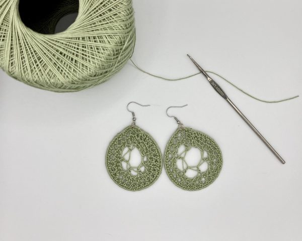 Crochet green dream catcher earrings laying next to a ball of green yarn and a crochet hook