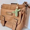 Crocheted green cactus bag charm with pearl accent and gold key ring on a brown purse