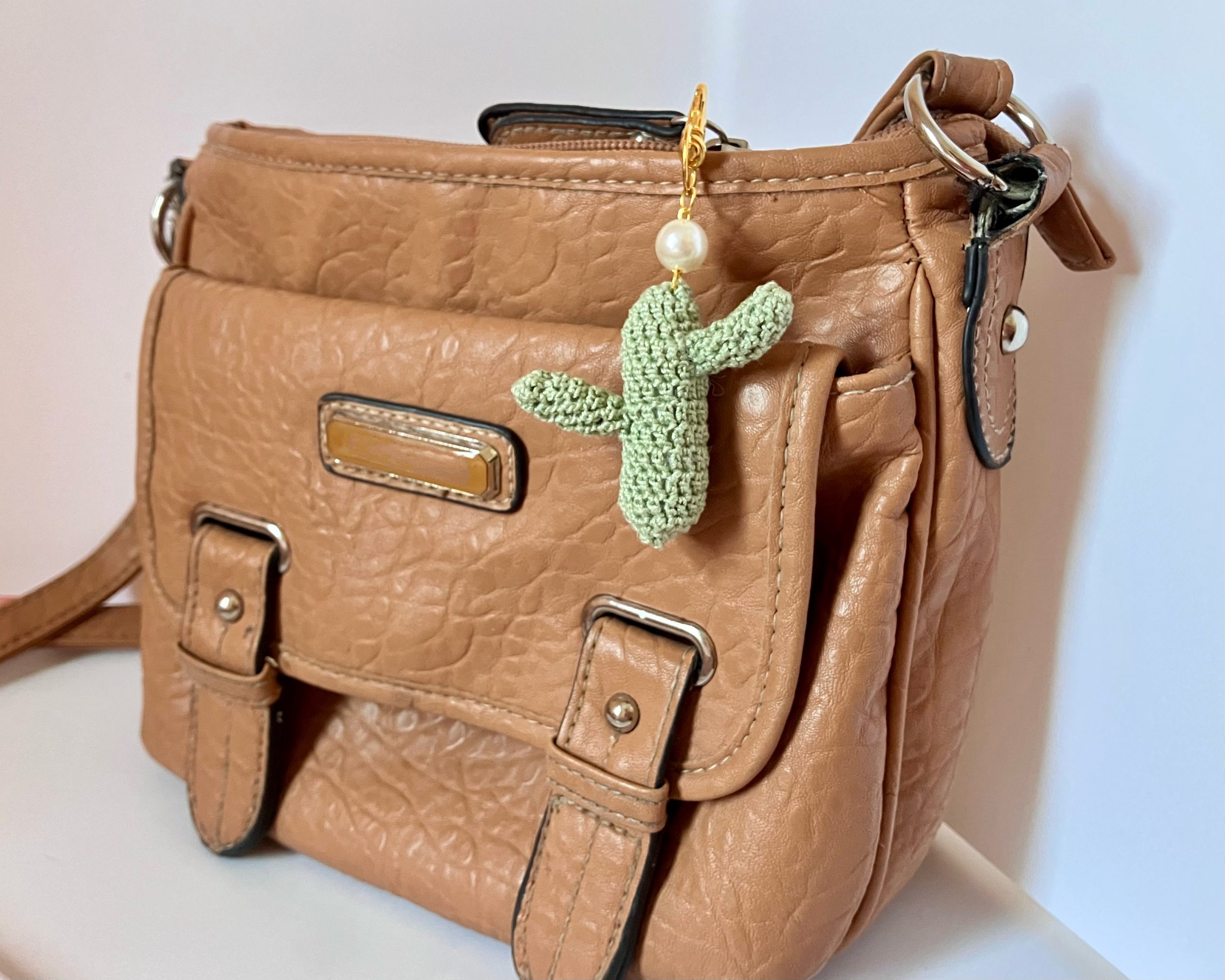 Crocheted green cactus bag charm with pearl accent and gold key ring on a brown purse