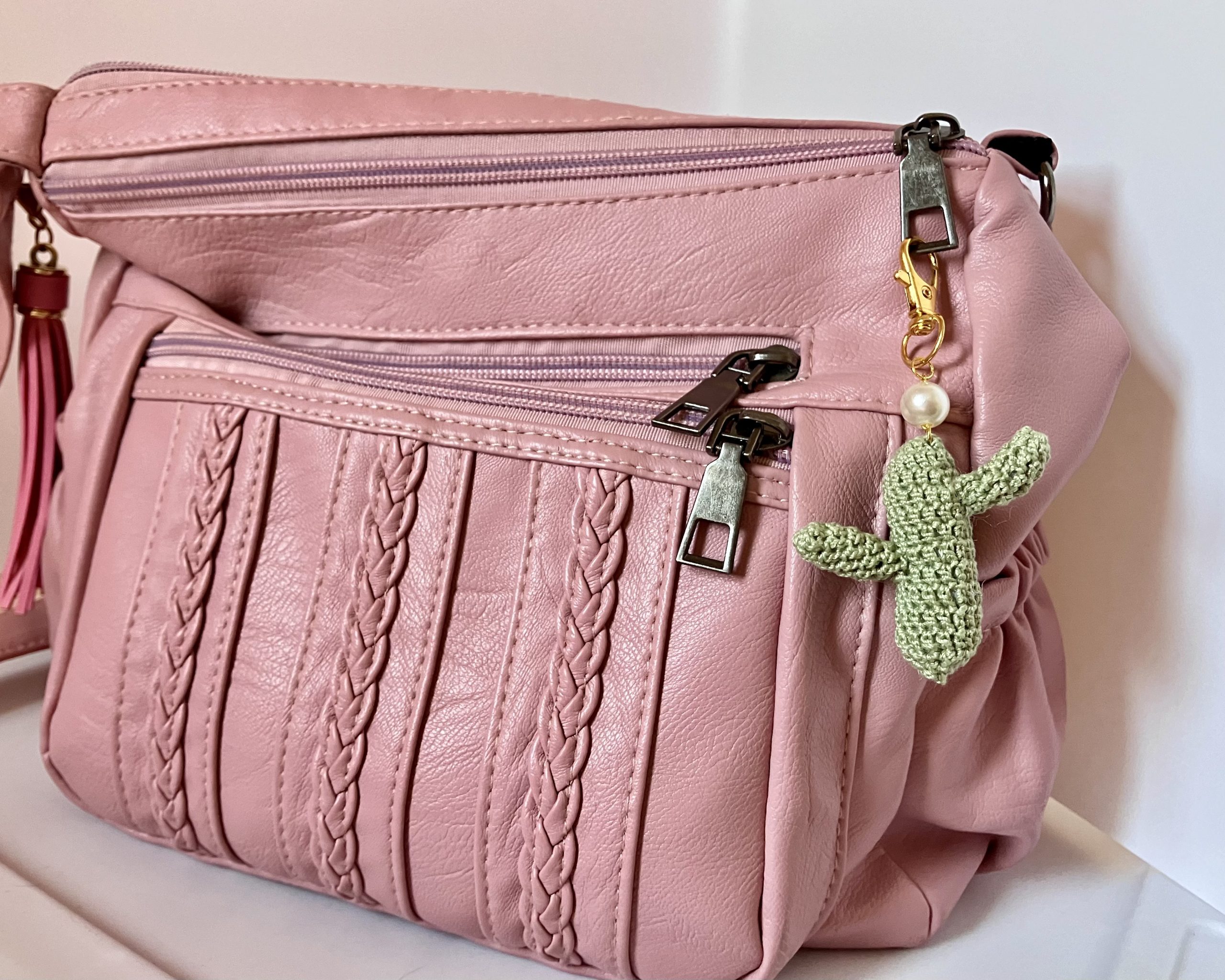 Crocheted green cactus bag charm with pearl accent, on a gold key ring, hanging on a pink purse