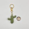 Crocheted green cactus with pearl accent, and gold key ring, next to a quarter for size reference