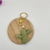 Crocheted green cactus with pearl accent, and gold key ring, on a wood coaster