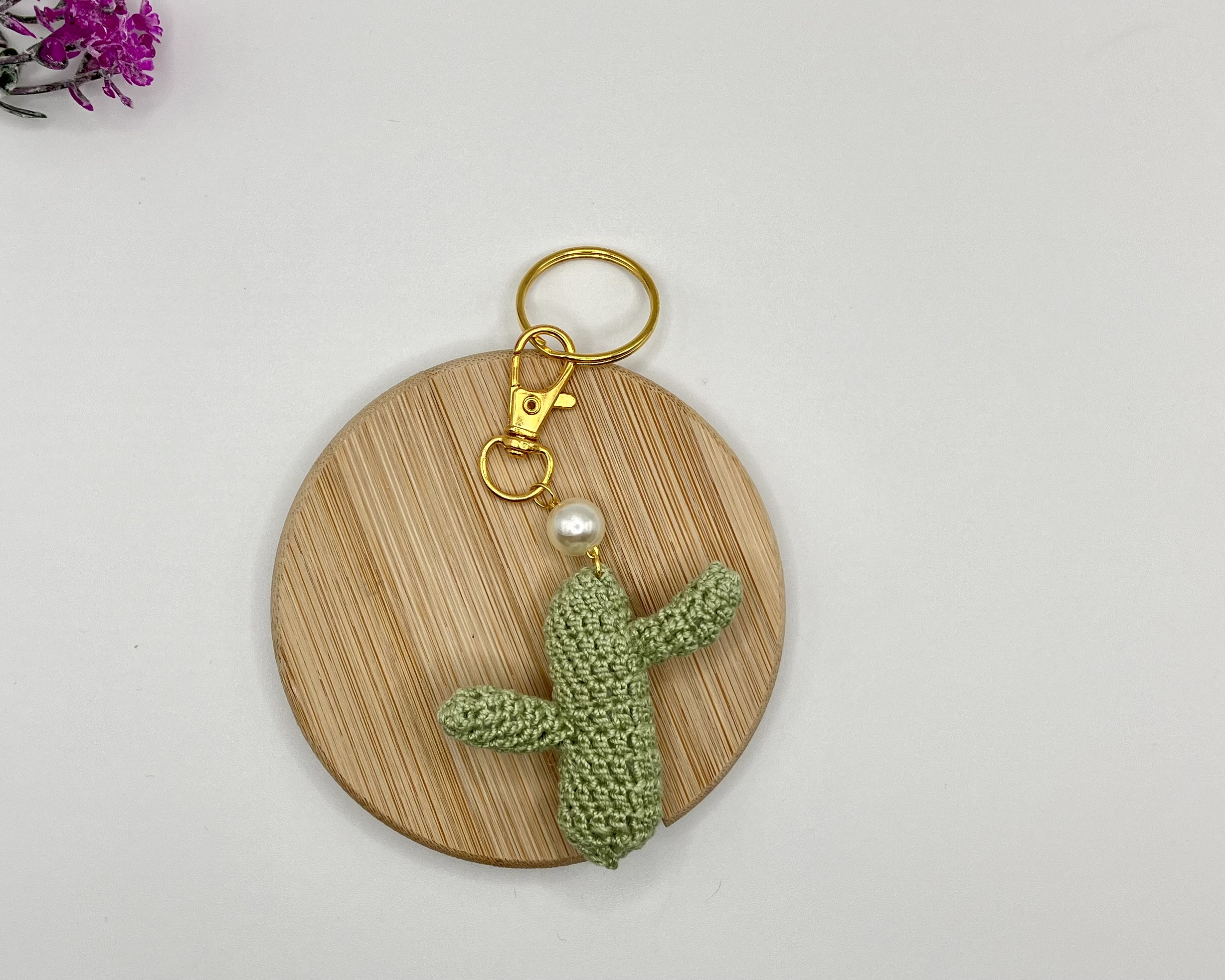 Crocheted green cactus with pearl accent, and gold key ring, on a wood coaster
