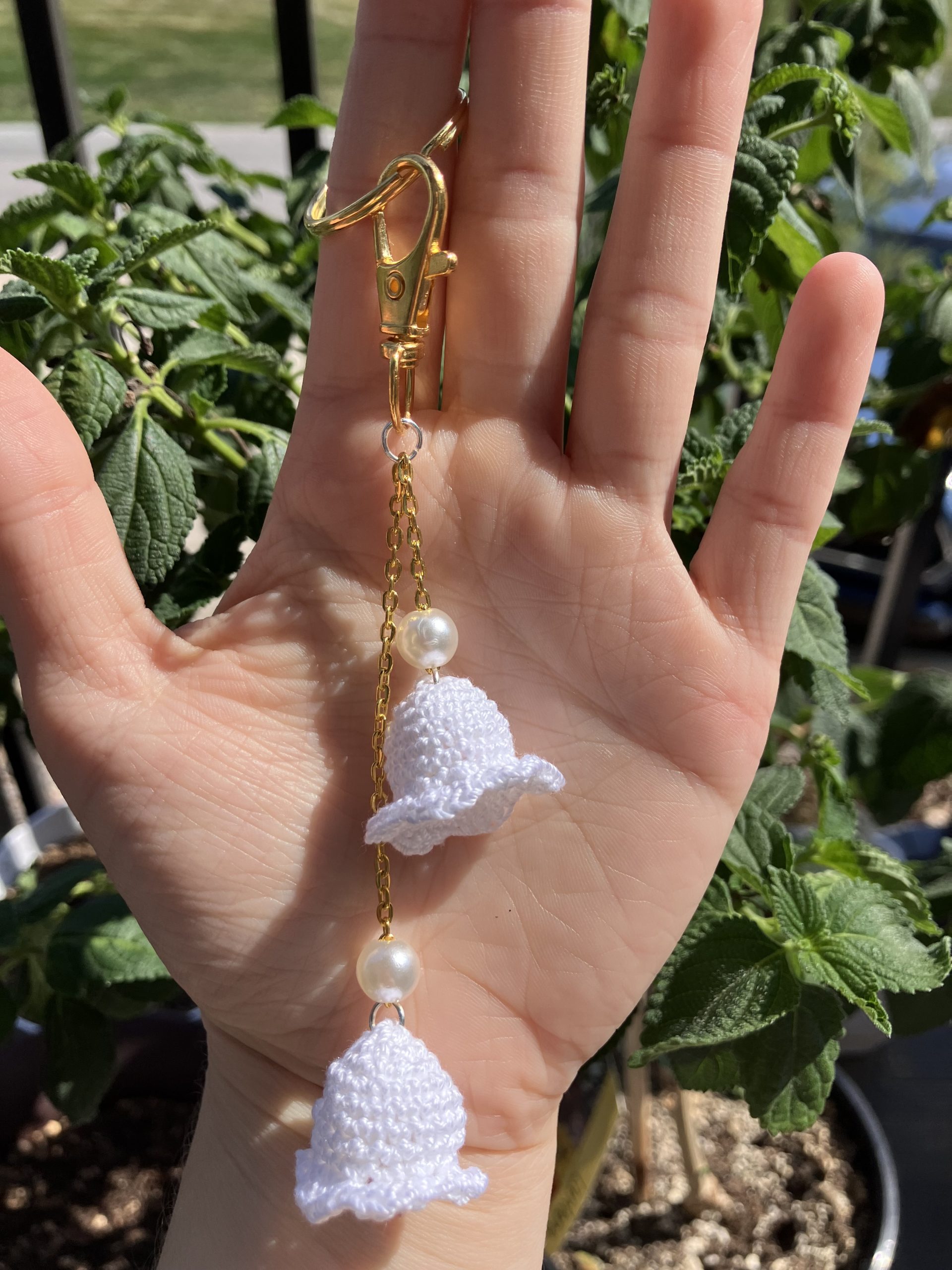 Lily bag charm with pearls on a gold chain, in a hand for reference