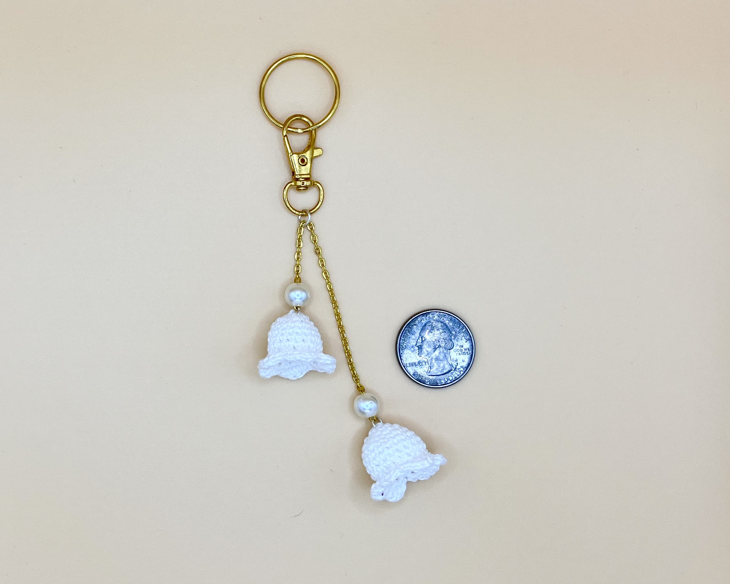Lily bag charm with pearls on a gold chain, next to a quarter for reference