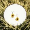 Crochet sunflower earrings, laying on a mirror, in lush green grass