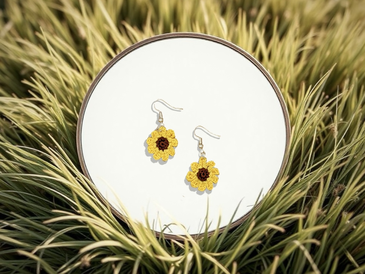 Crochet sunflower earrings, laying on a mirror, in lush green grass