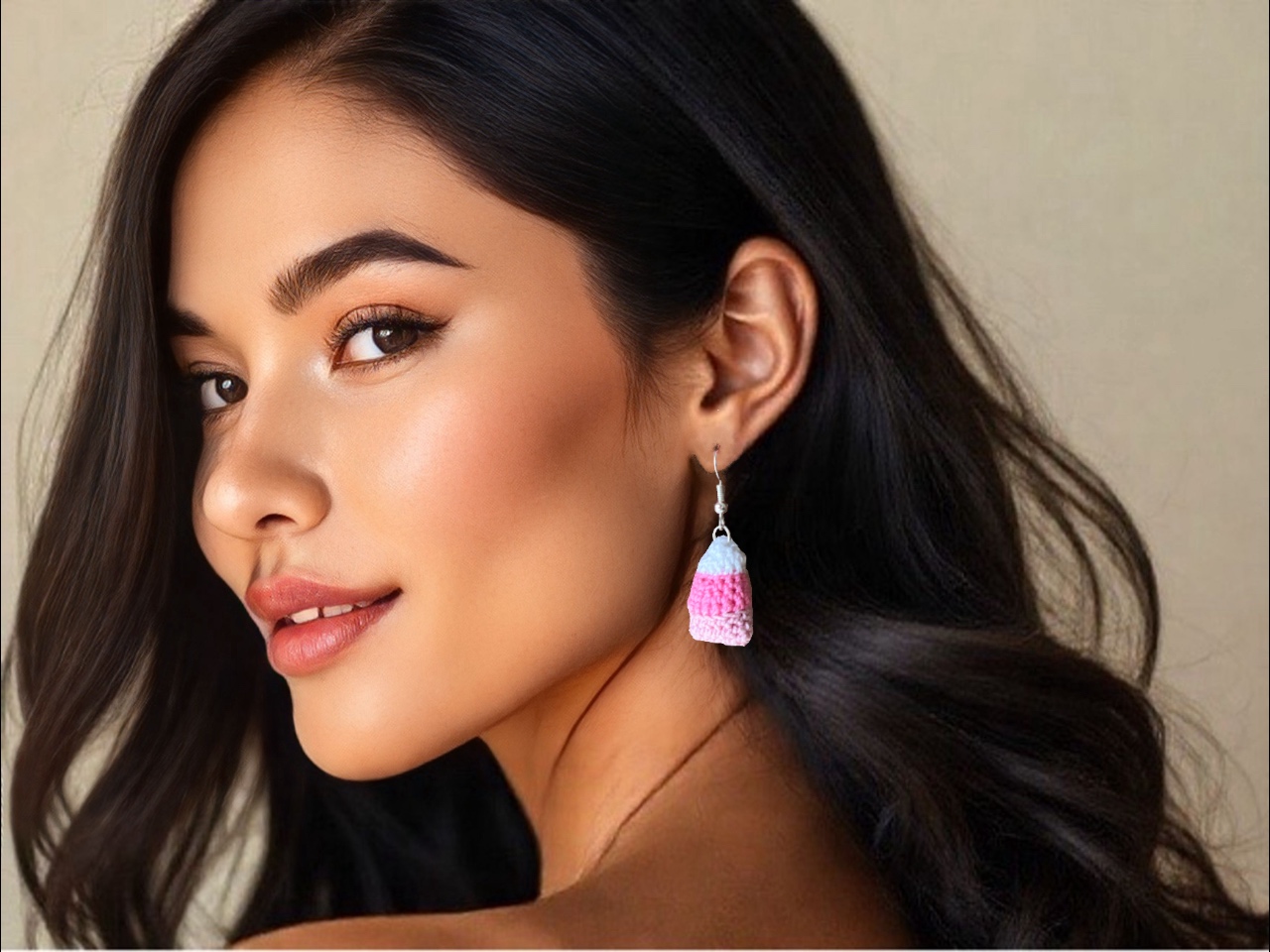 Dark haired woman, against a neutral backdrop, wearing handmade crochet pink candy corn earrings