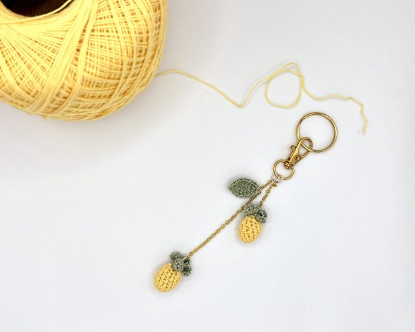 Crocheted pineapple bag charm next to a ball of yellow yarn