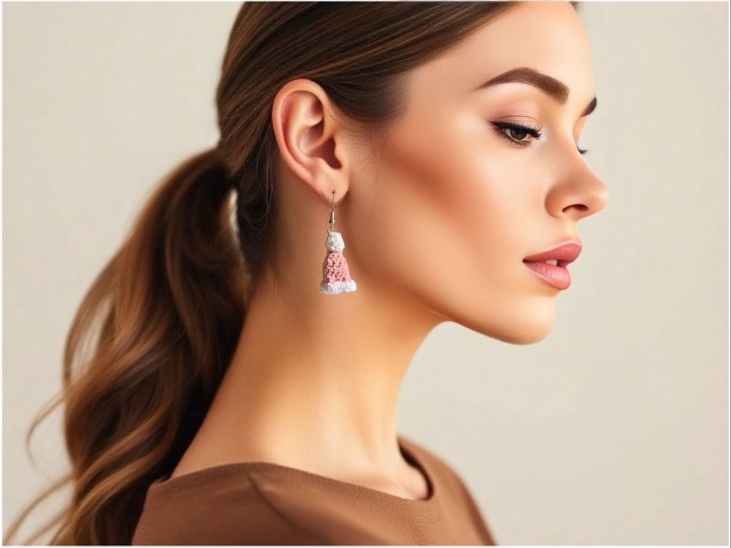 Profile image of a brown-haired model wearing handmade crochet pink Santa hat earrings, showcasing holiday-themed accessories against a neutral background.