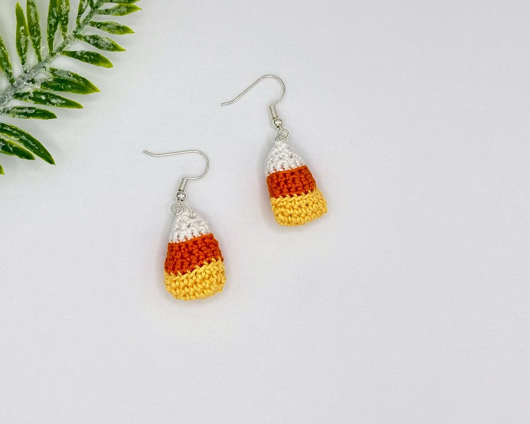 Crochet candy corn earrings laying flat on a white backdrop