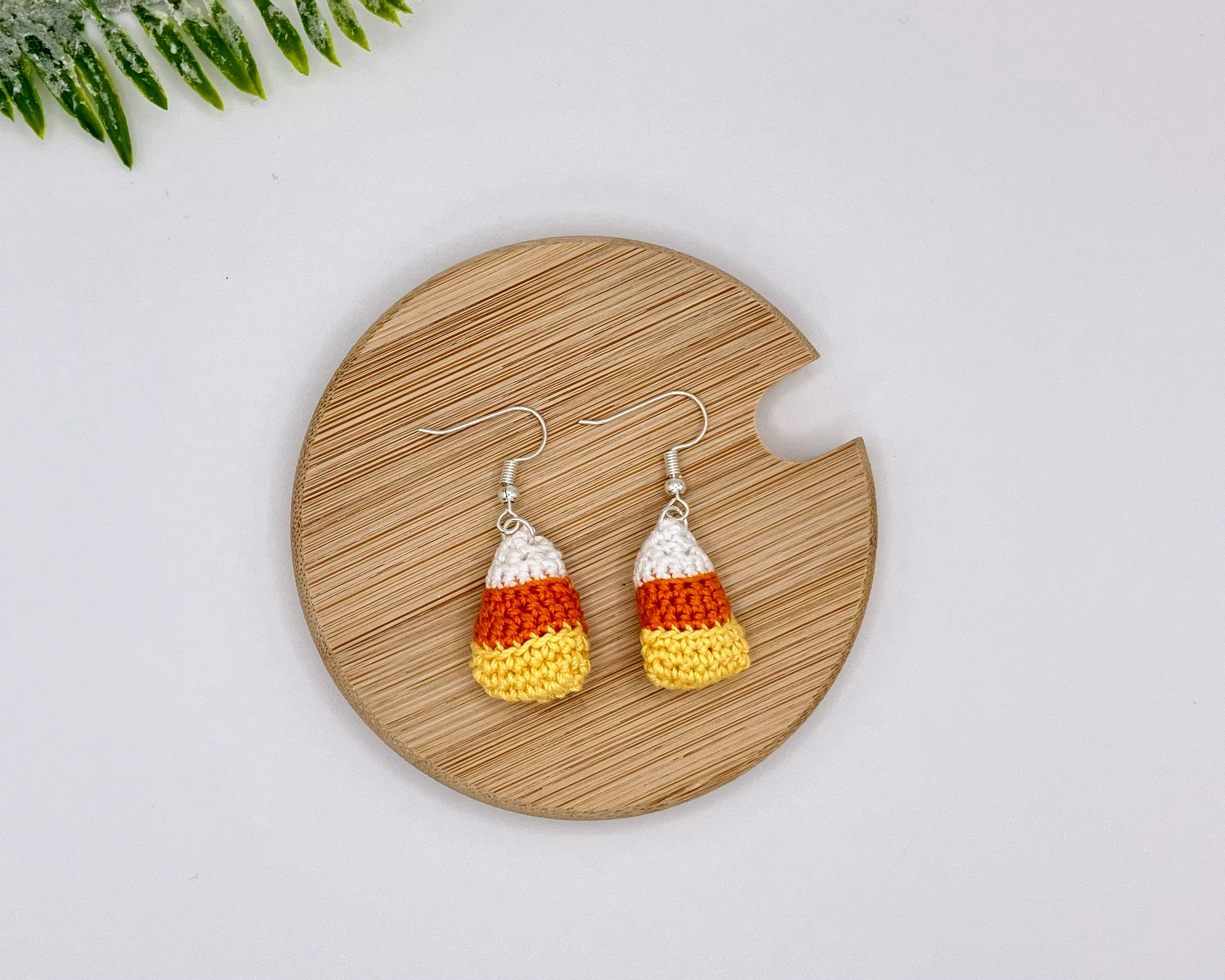 Crochet candy corn earrings laying flat on a wood backdrop