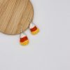 Crochet candy corn earrings with the hooks resting on a wood backdrop