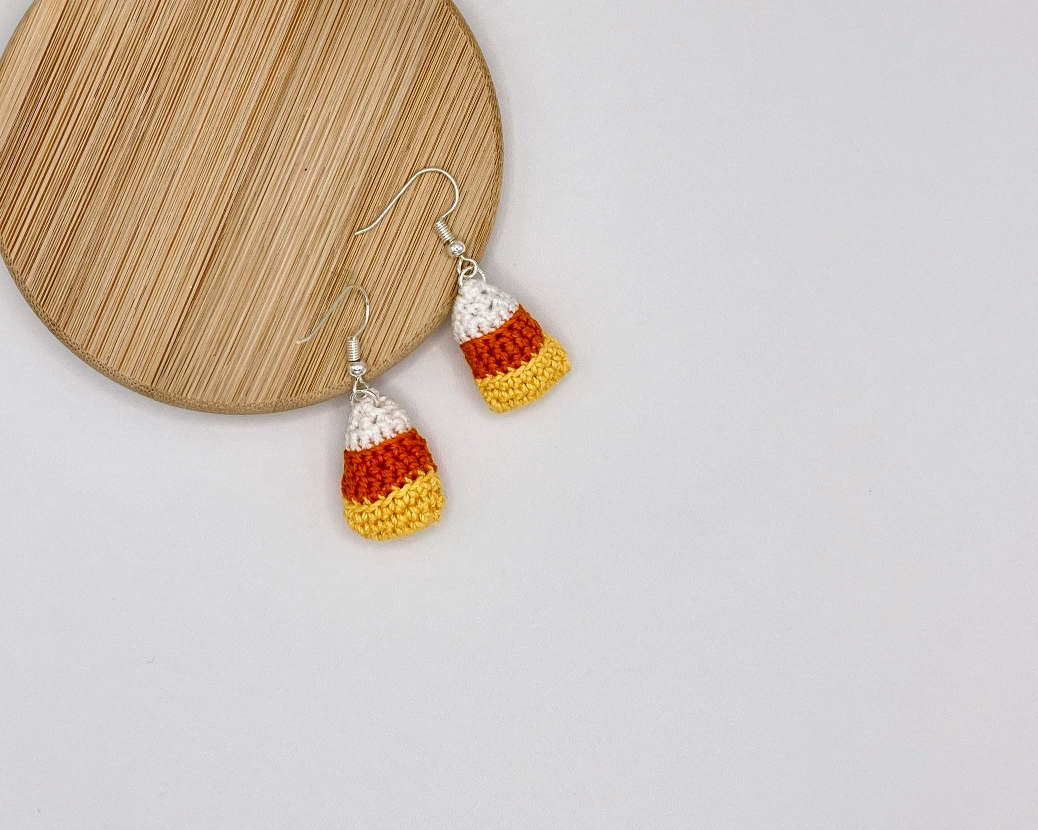 Crochet candy corn earrings with the hooks resting on a wood backdrop