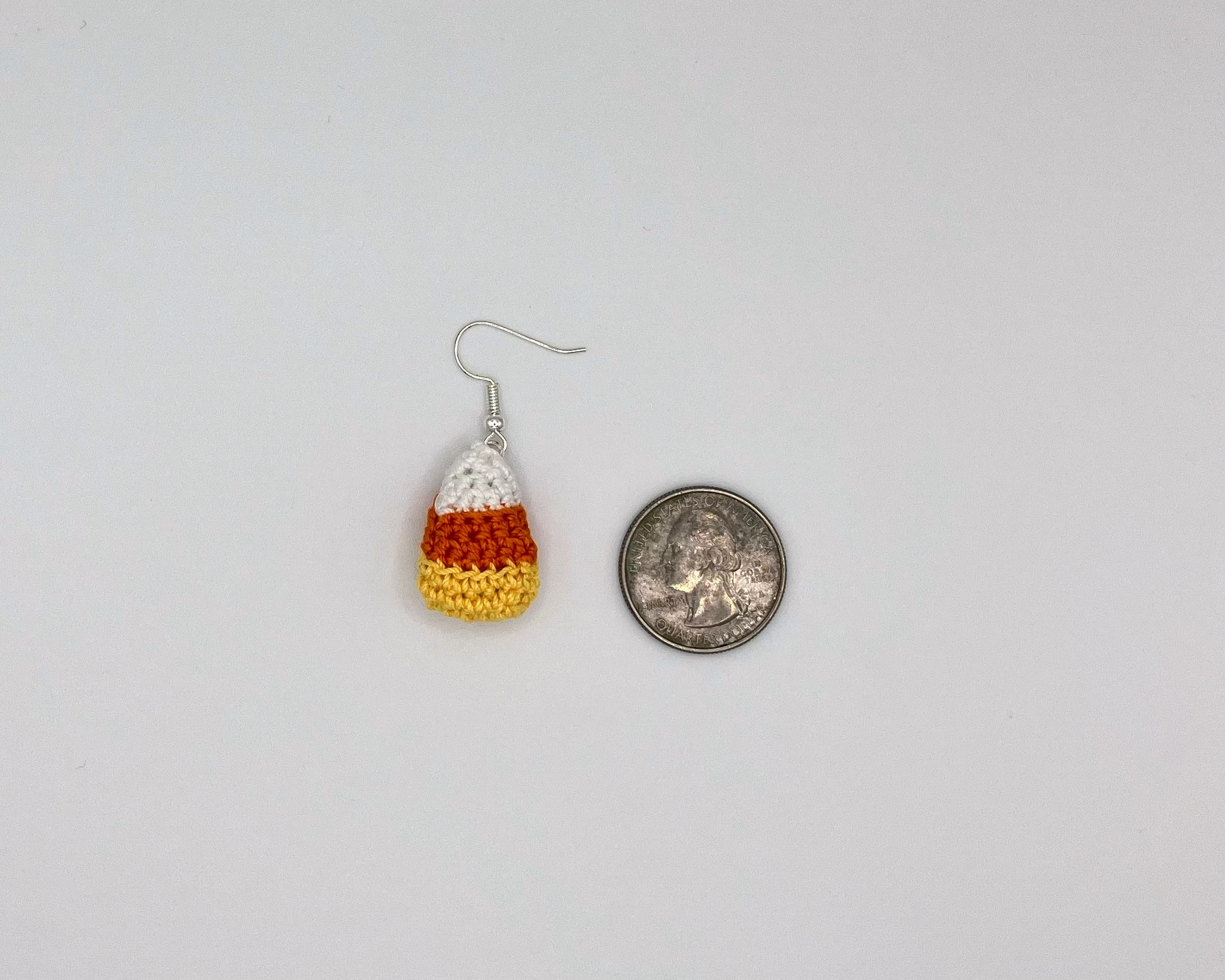 Candy corn earring laying next to a quarter for reference