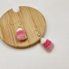 Crocheted pink candy corn earrings one laying on a wood coaster and one on a white backdrop