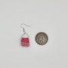 Crocheted pink candy corn earring laying next to a quarter for size reference