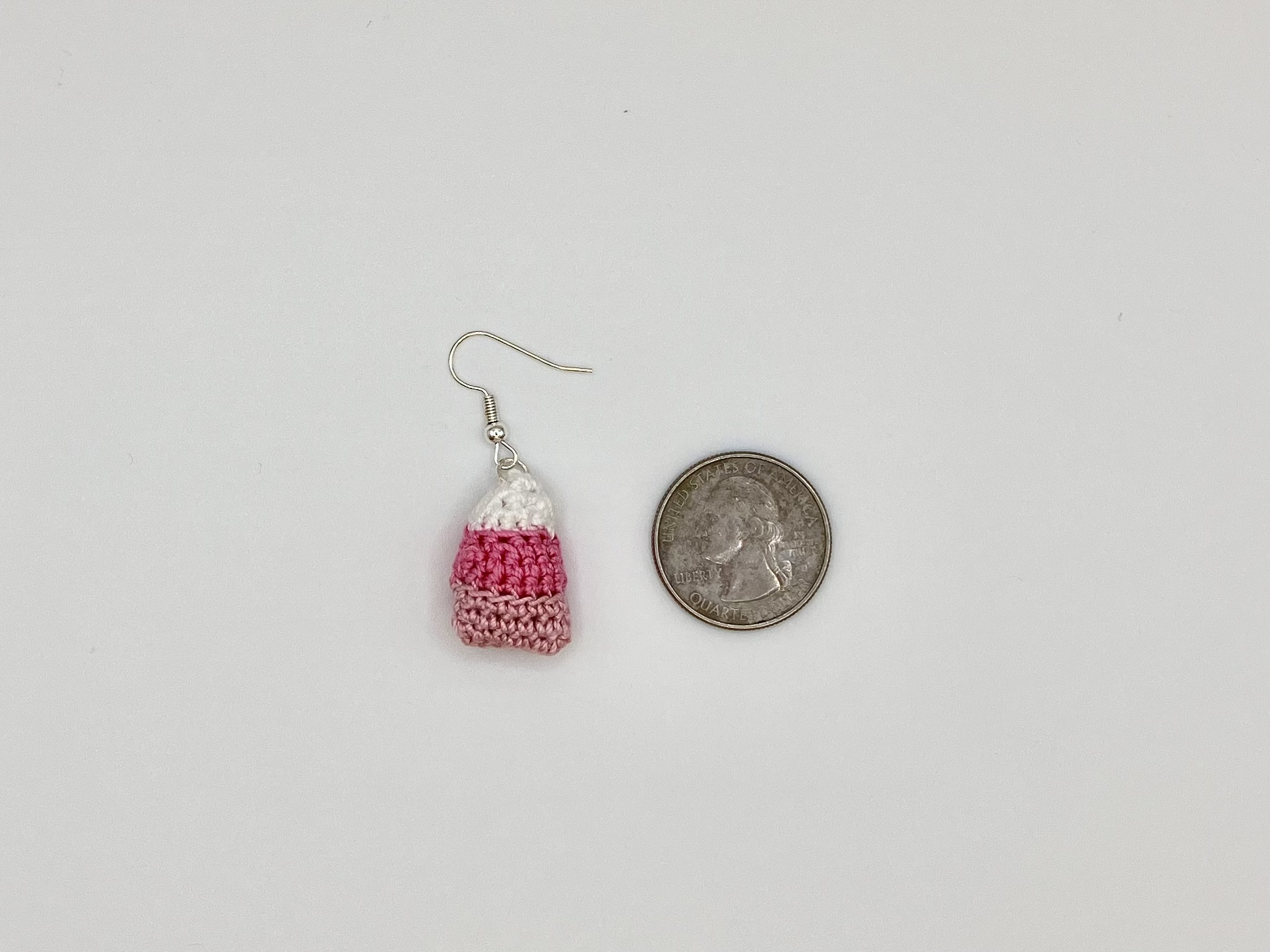 Crocheted pink candy corn earring laying next to a quarter for size reference