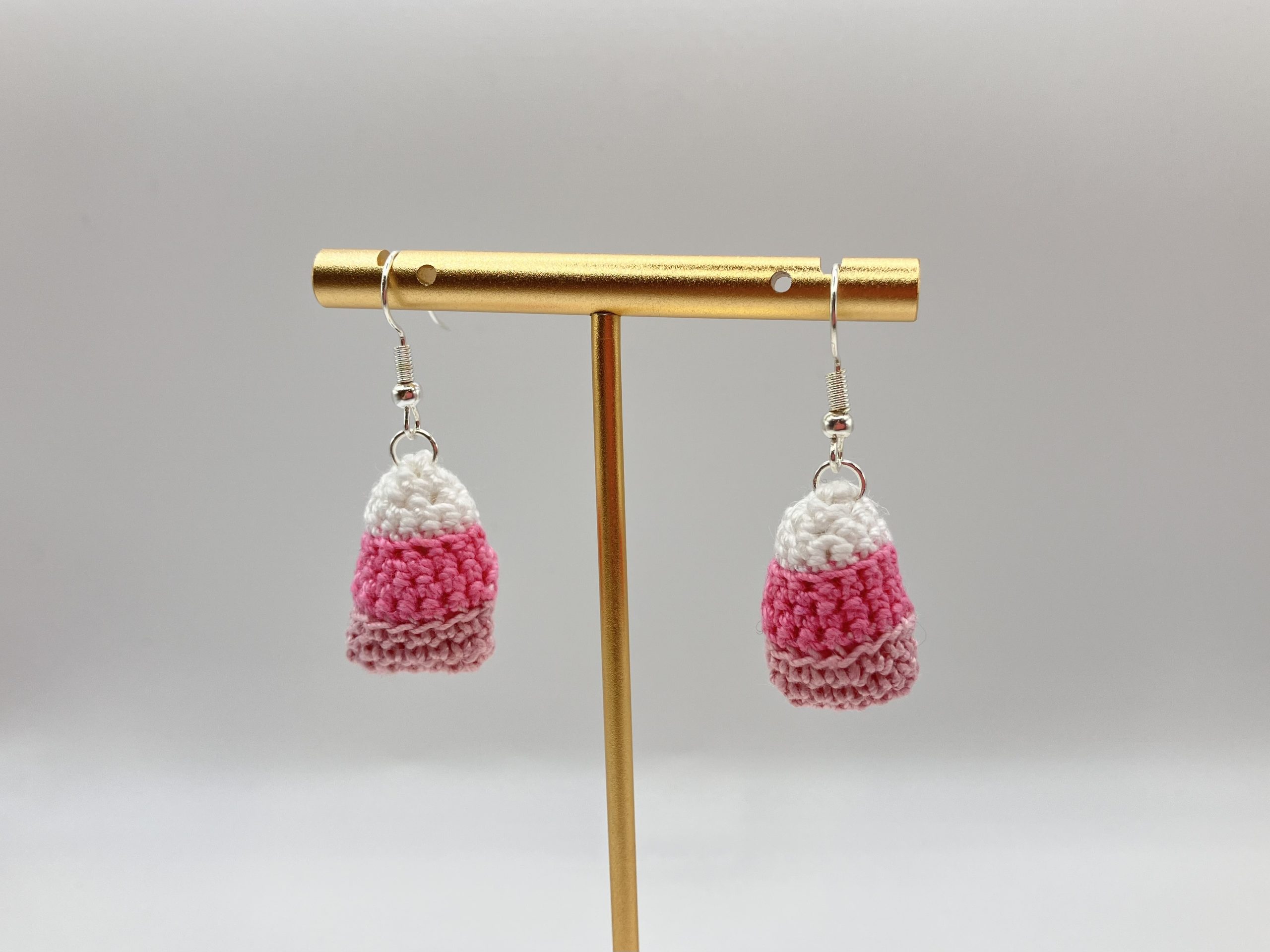 Crocheted pink candy corn earrings handing on a gold earring stand